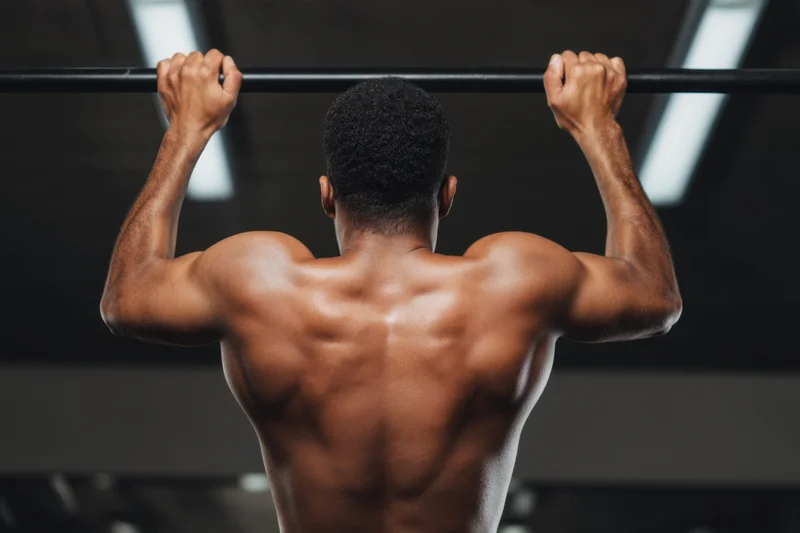 Muscular man doing pull-up on ceiling-mounted bar in gym