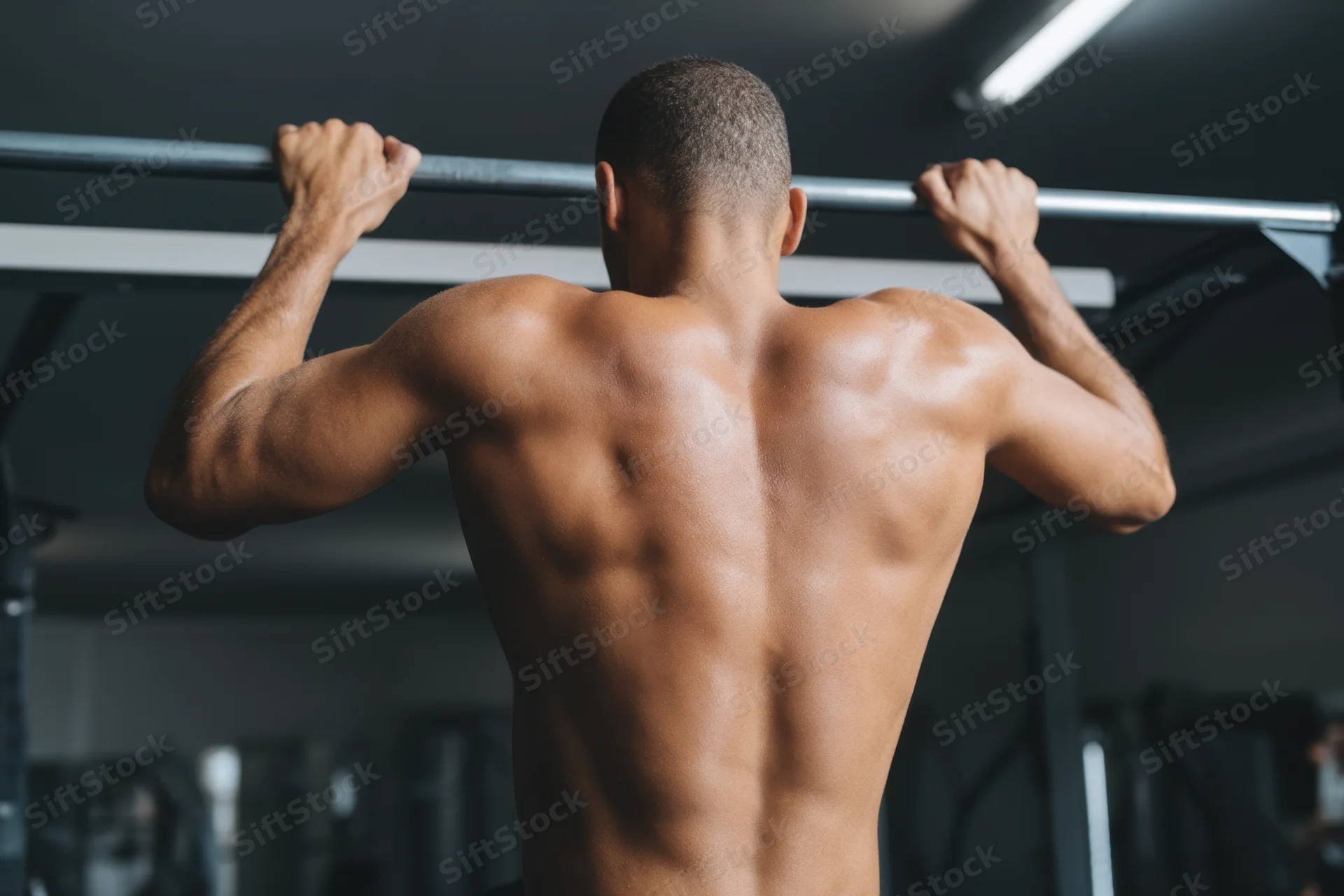 Muscular man doing pull-up on ceiling-mounted bar in gym