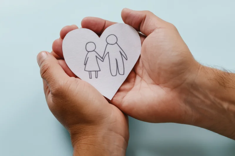 Hands cradling a paper heart with a simple drawing of a couple holding hands