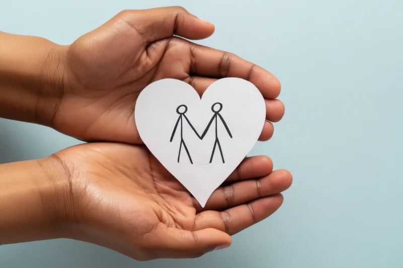 Adult hands cradling a paper heart with a stick figure couple drawing against a light blue background