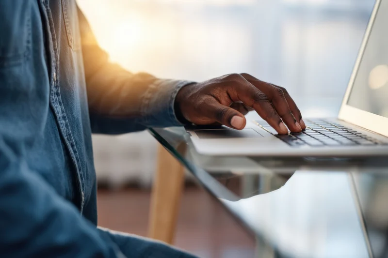Man typing on laptop at glass desk with sunlight glowing behind