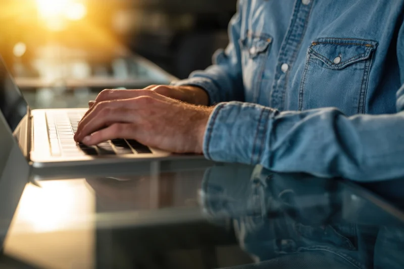 Man typing on laptop at glass desk in office setting