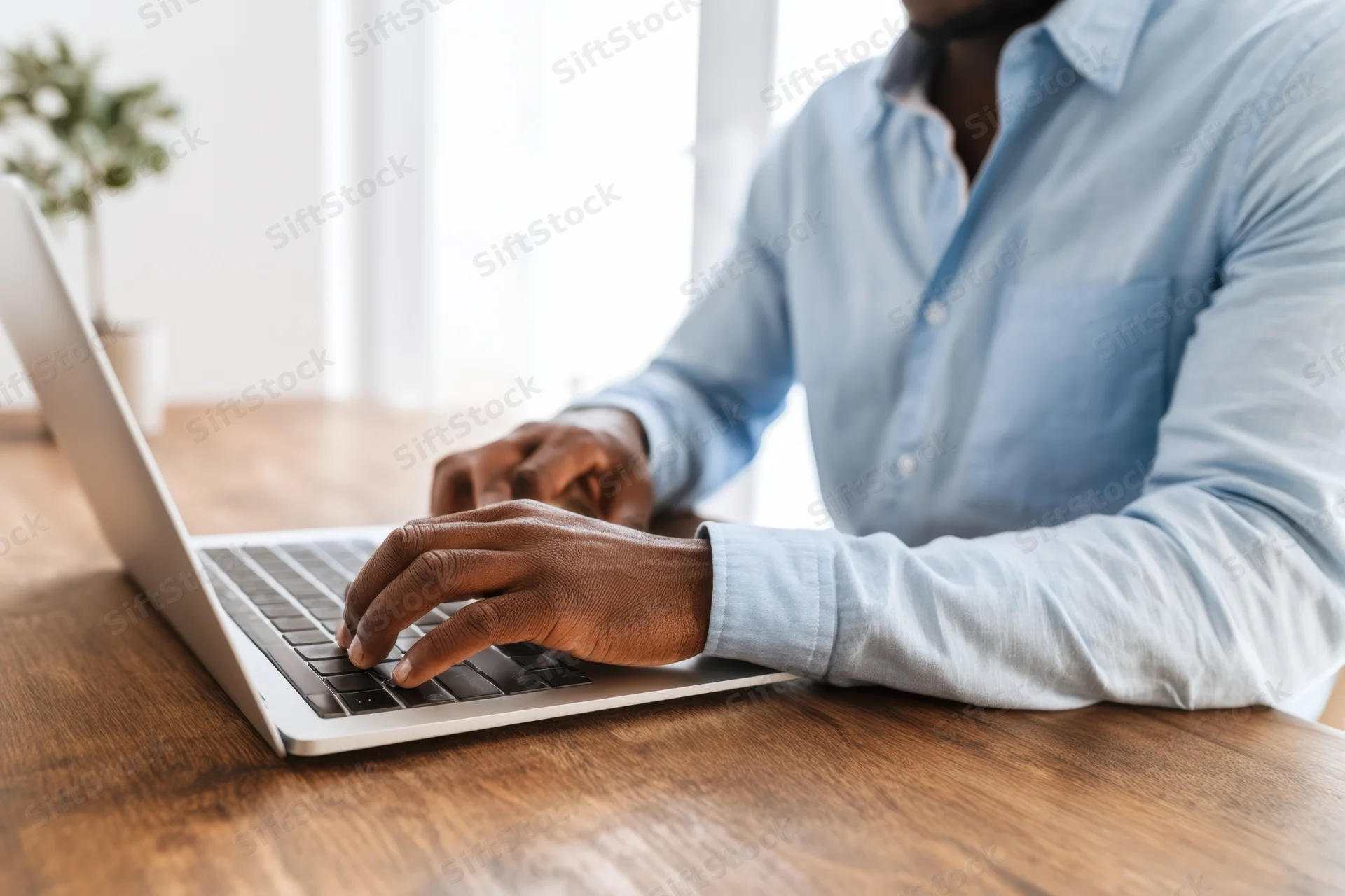 Man typing on laptop at wooden desk in bright office space