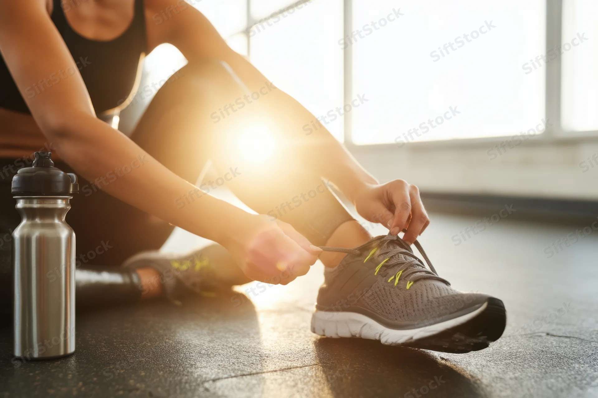 Woman tying shoelace on gym floor with water bottle beside her