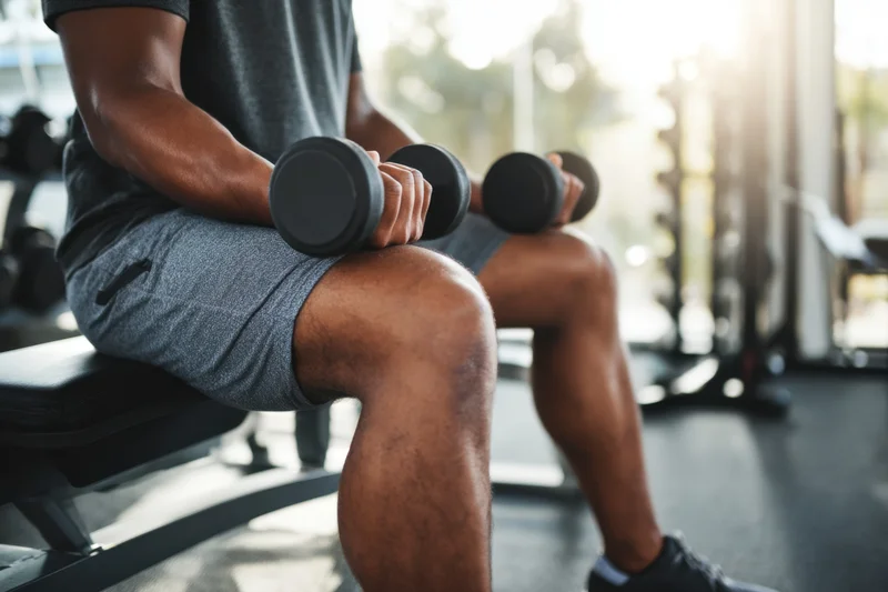 Man seated on gym bench holding dumbbells for strength training