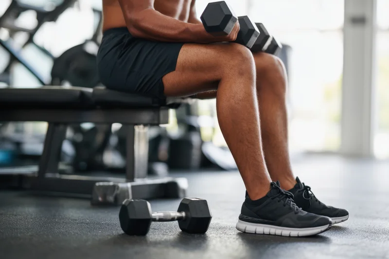 Man performing seated dumbbell curl on gym bench with weights in hand