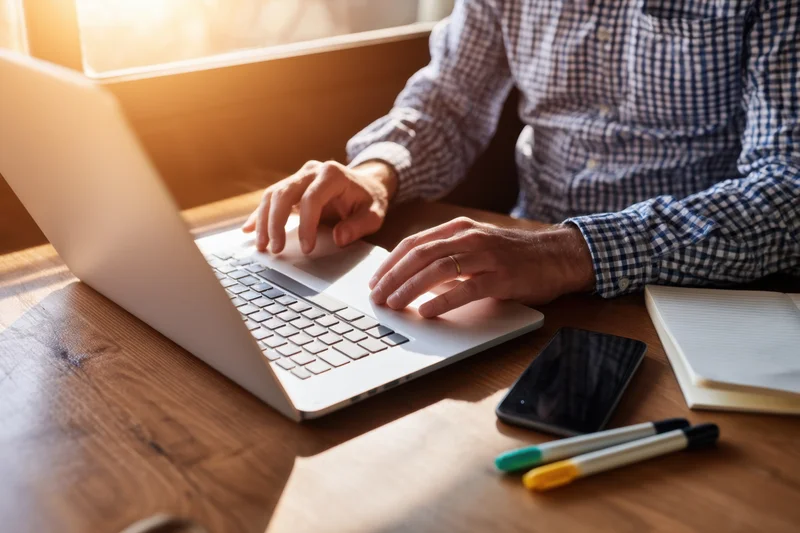 Man typing on laptop at wooden desk in sunlit home office