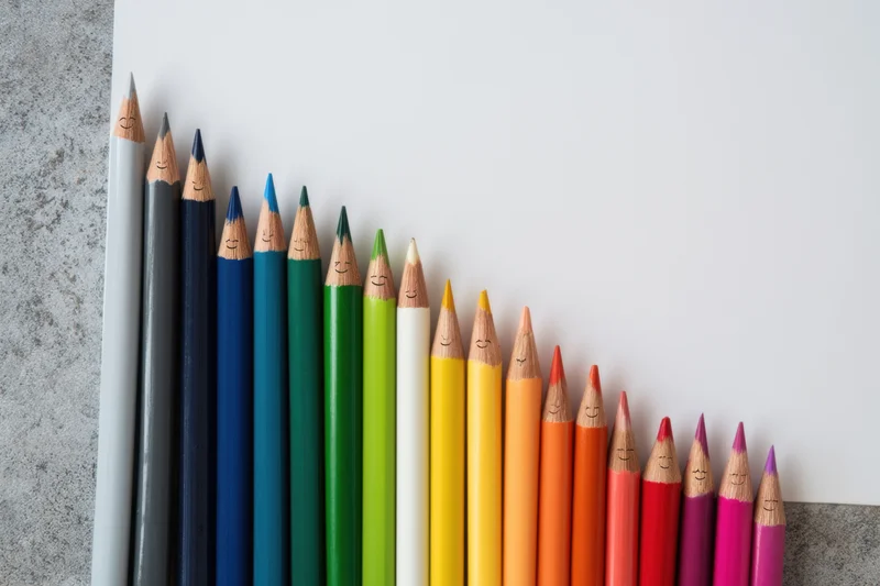 Row of colored pencils with smiling faces arranged in gradient on desk surface