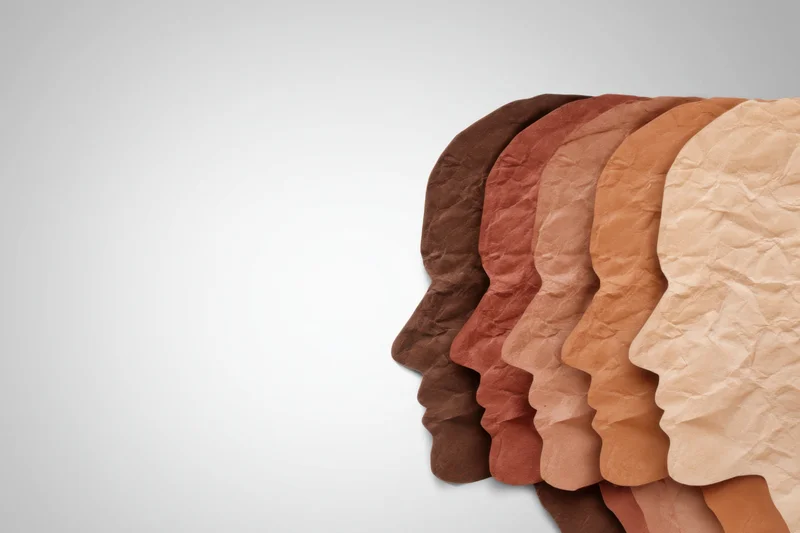 Row of crumpled paper head silhouettes in various skin tones against white background