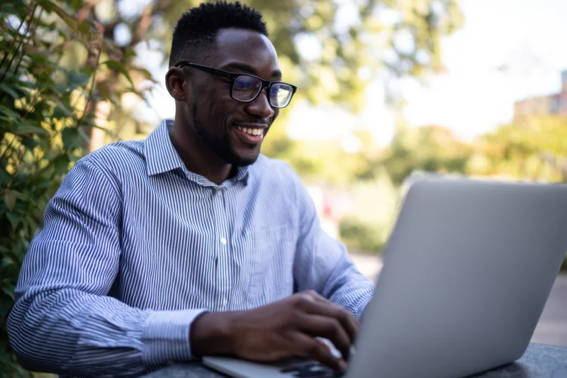 Smiling man typing on laptop outdoors in a park setting