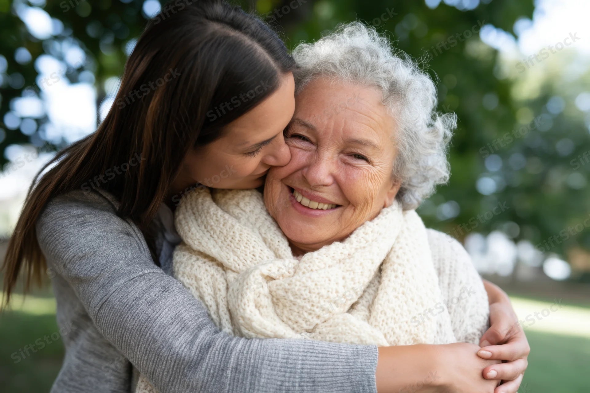 Younger woman hugging senior woman in a park, both smiling warmly