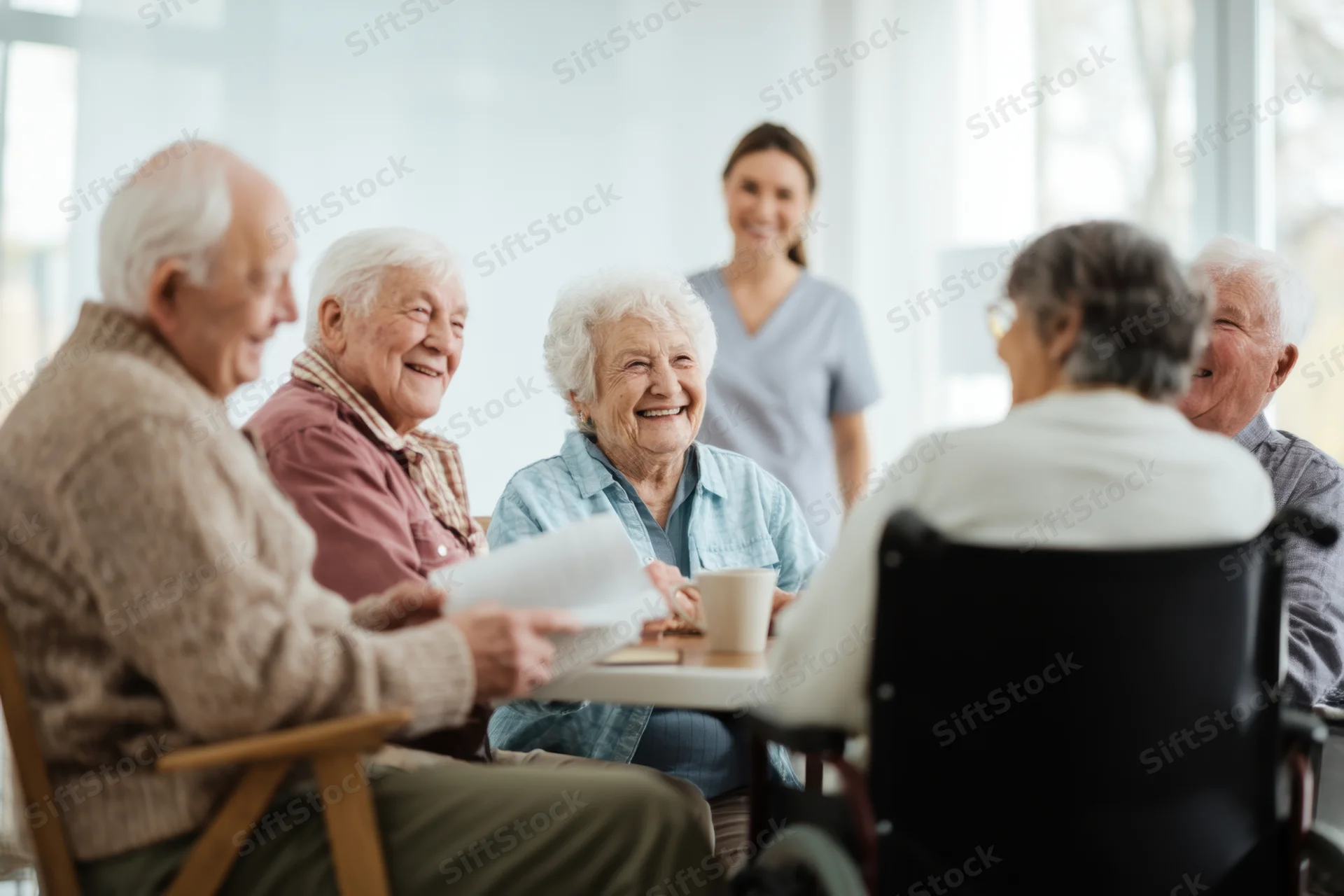 Elderly people smiling and interacting around a table in a bright living room with a caregiver present