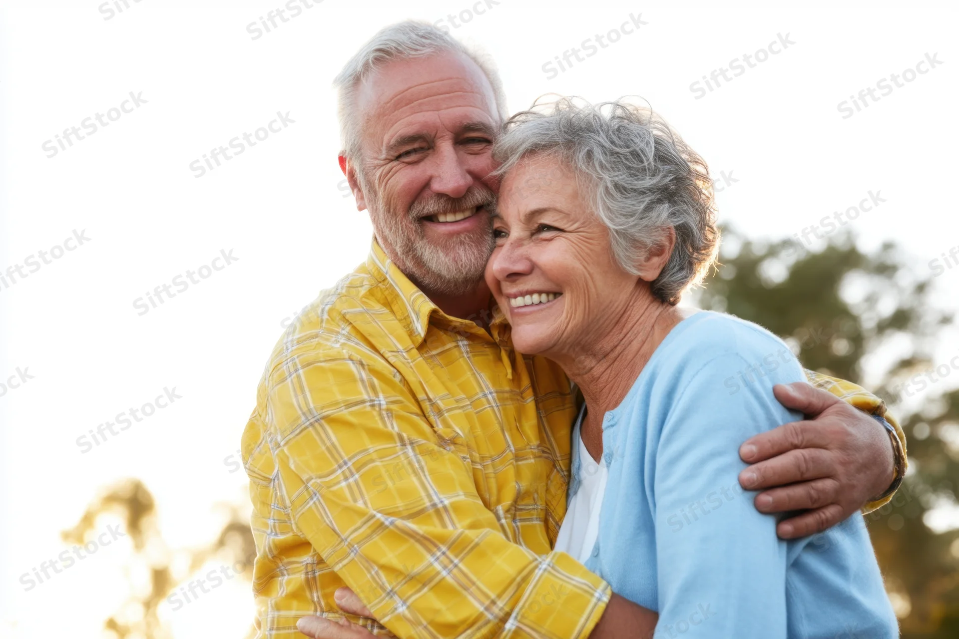 Elderly couple hugging and smiling outdoors in sunlight