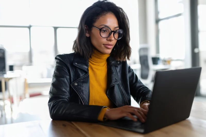 Woman typing on laptop at wooden desk in bright office space