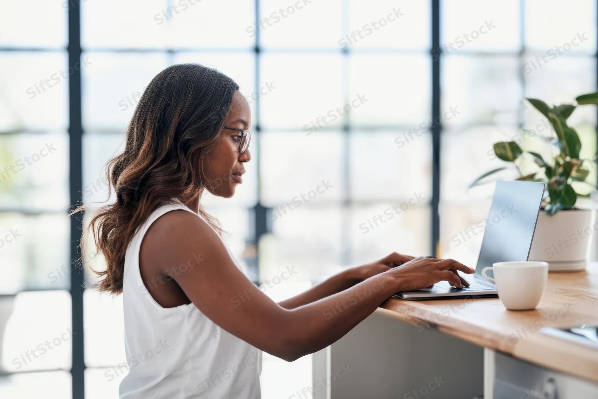 African woman working on laptop at desk in bright modern office space