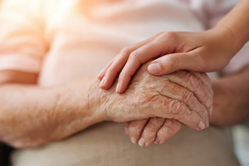 Elderly woman's wrinkled hands being held by a young child's hand in a close-up indoor setting