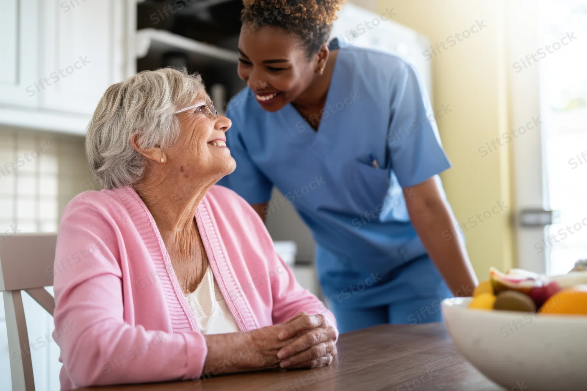 Elderly woman smiling at caregiver in kitchen during conversation
