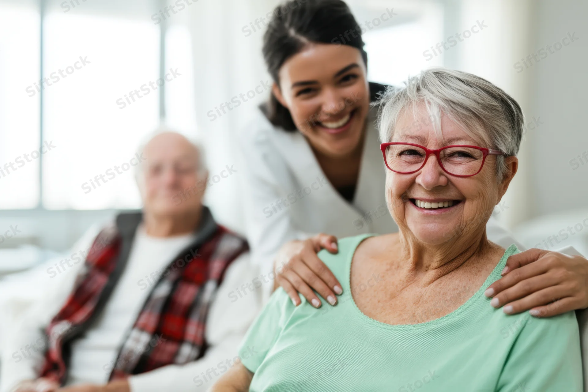 Elderly woman smiling with red glasses as caregiver places hands on her shoulders in a bright living room