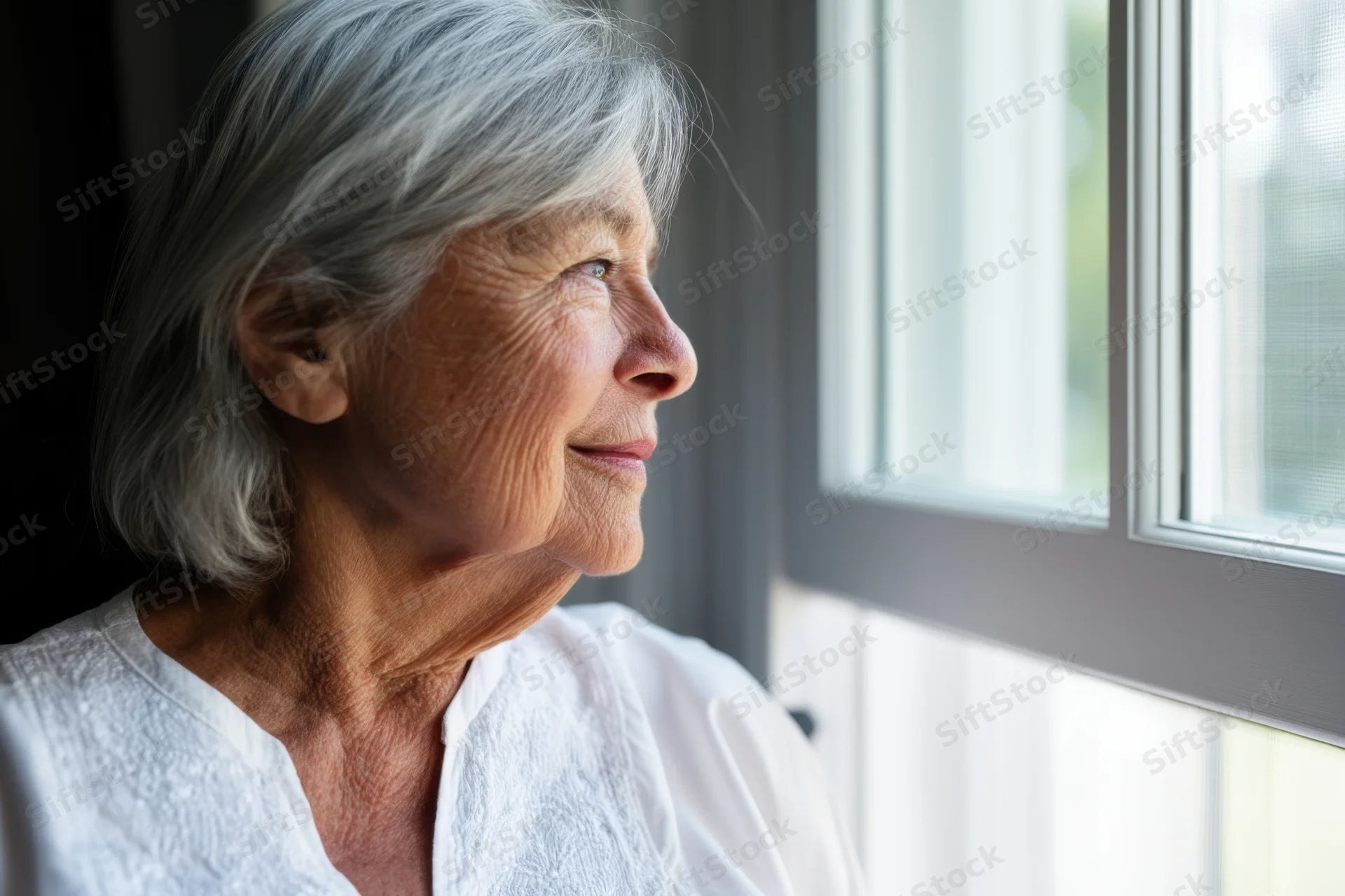 Elderly woman in profile looking out window in soft natural light