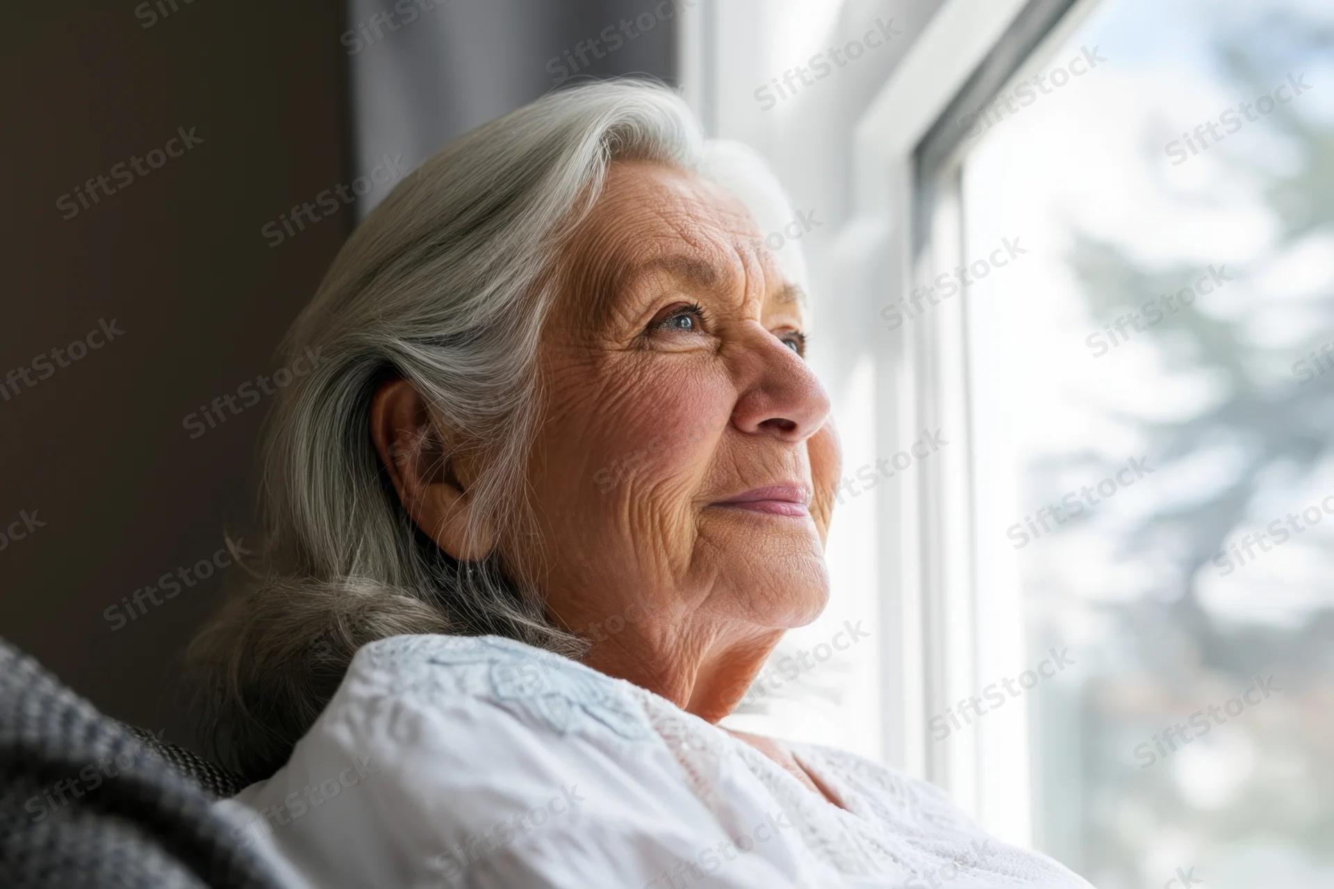 Elderly woman with silver hair looking out window in home setting