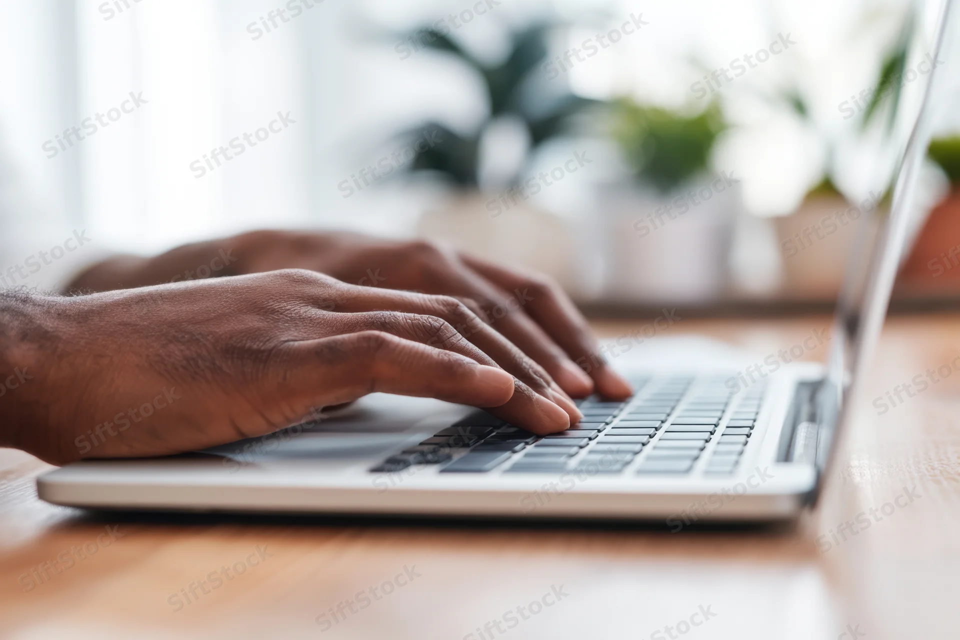 Hands typing on a laptop keyboard on a wooden desk