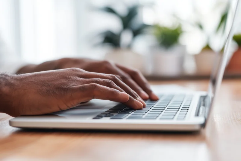 Hands typing on a laptop keyboard on a wooden desk