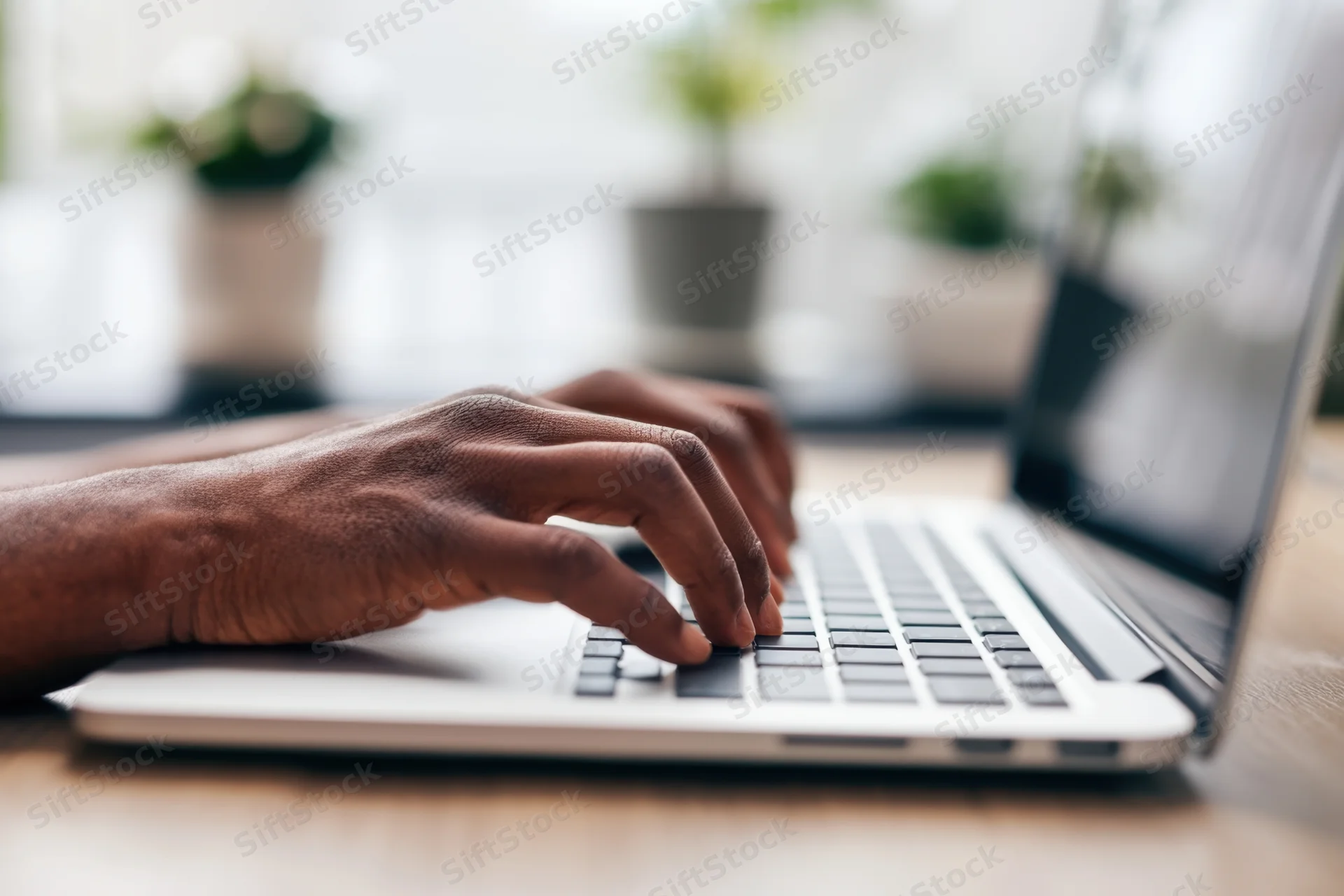 Hands typing on a laptop keyboard on a wooden desk