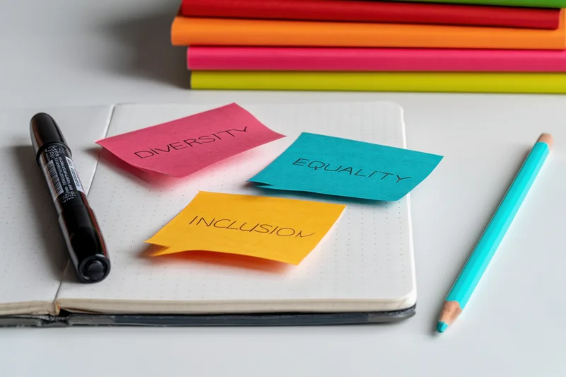 Colorful sticky notes with diversity equality inclusion text on open notebook with pencil and marker on desk