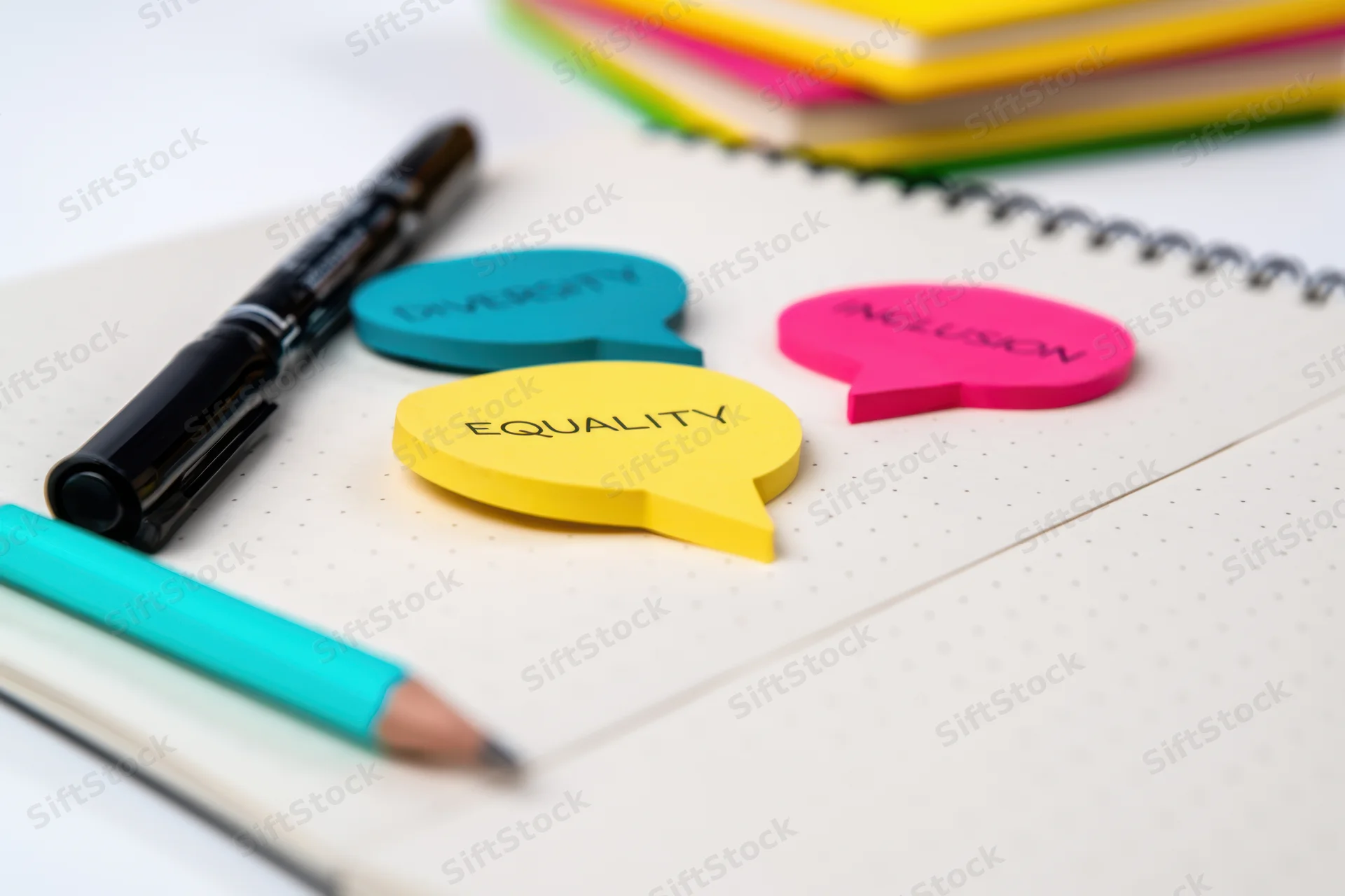 Colorful speech bubble notes with diversity equality inclusion text on a notebook with pens and pencils in an office workspace