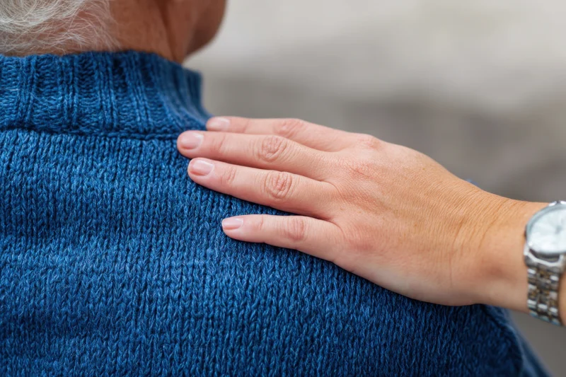 Hand resting on the shoulder of an elderly woman in a blue knit sweater