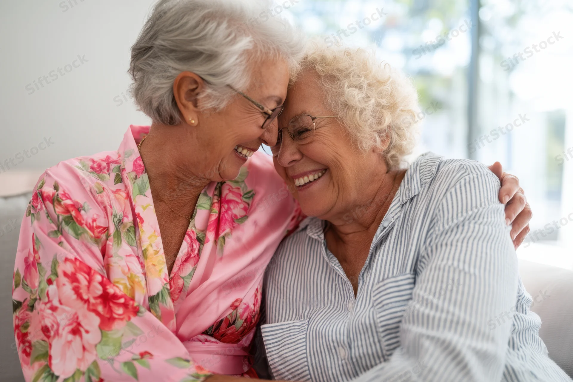 Two elderly women embracing and smiling together on a couch in a living room