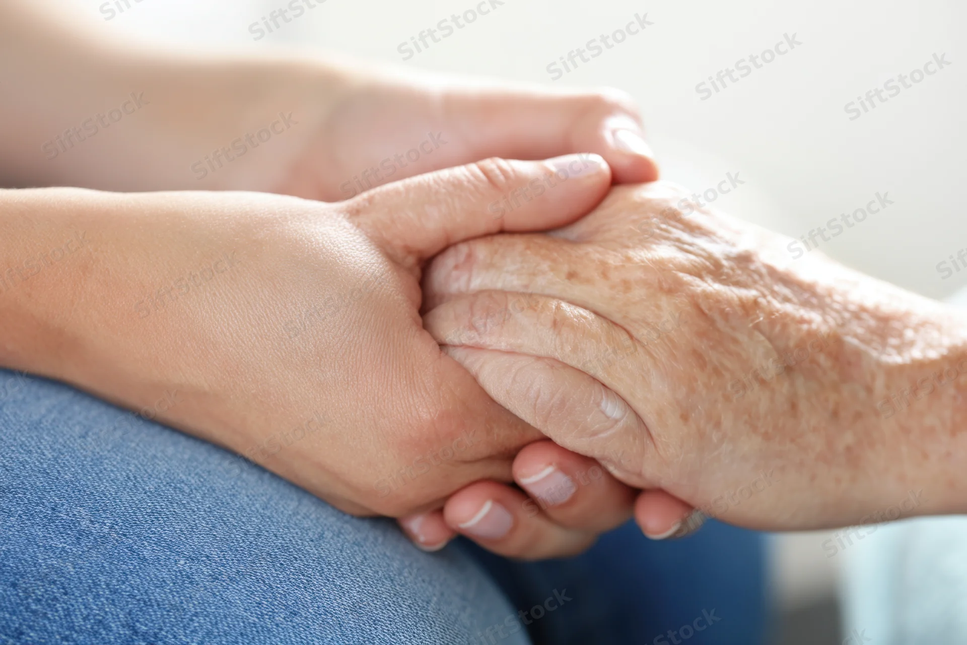 Younger hands gently holding an elderly person's hand in a close-up view