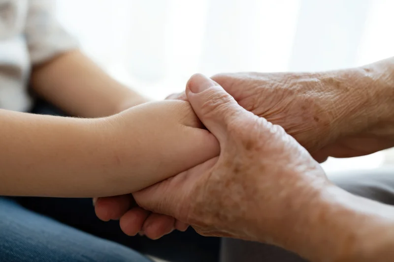 Elderly and young hands clasped in a tender hold indoors