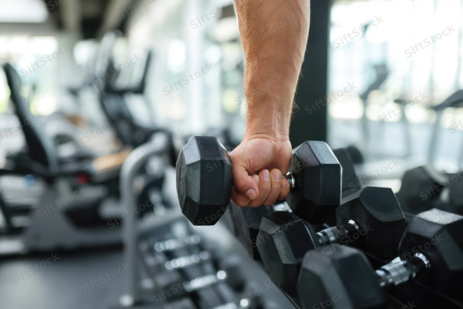 Close-up of a muscular arm gripping a dumbbell from a rack in a gym