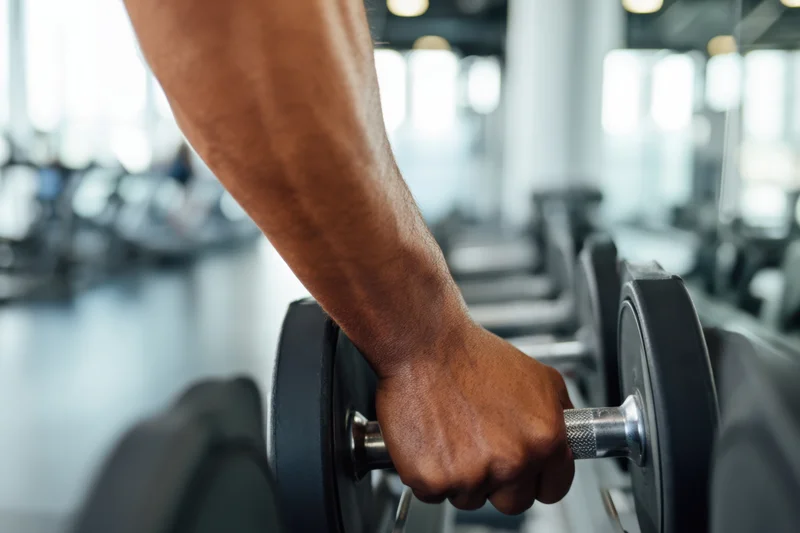Close-up of a man's arm gripping a dumbbell in a gym