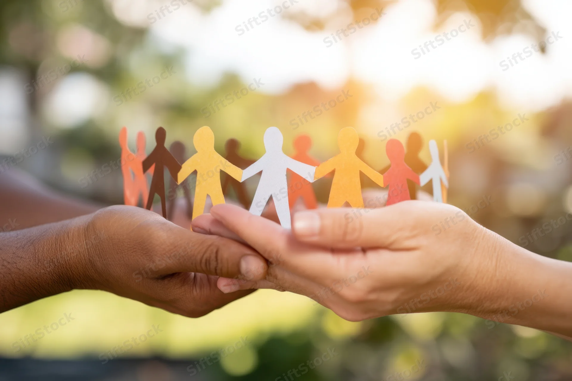 Two hands holding a colorful paper chain of human figures outdoors