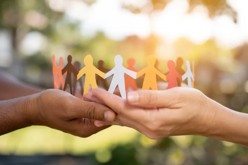 Two hands holding a colorful paper chain of human figures outdoors