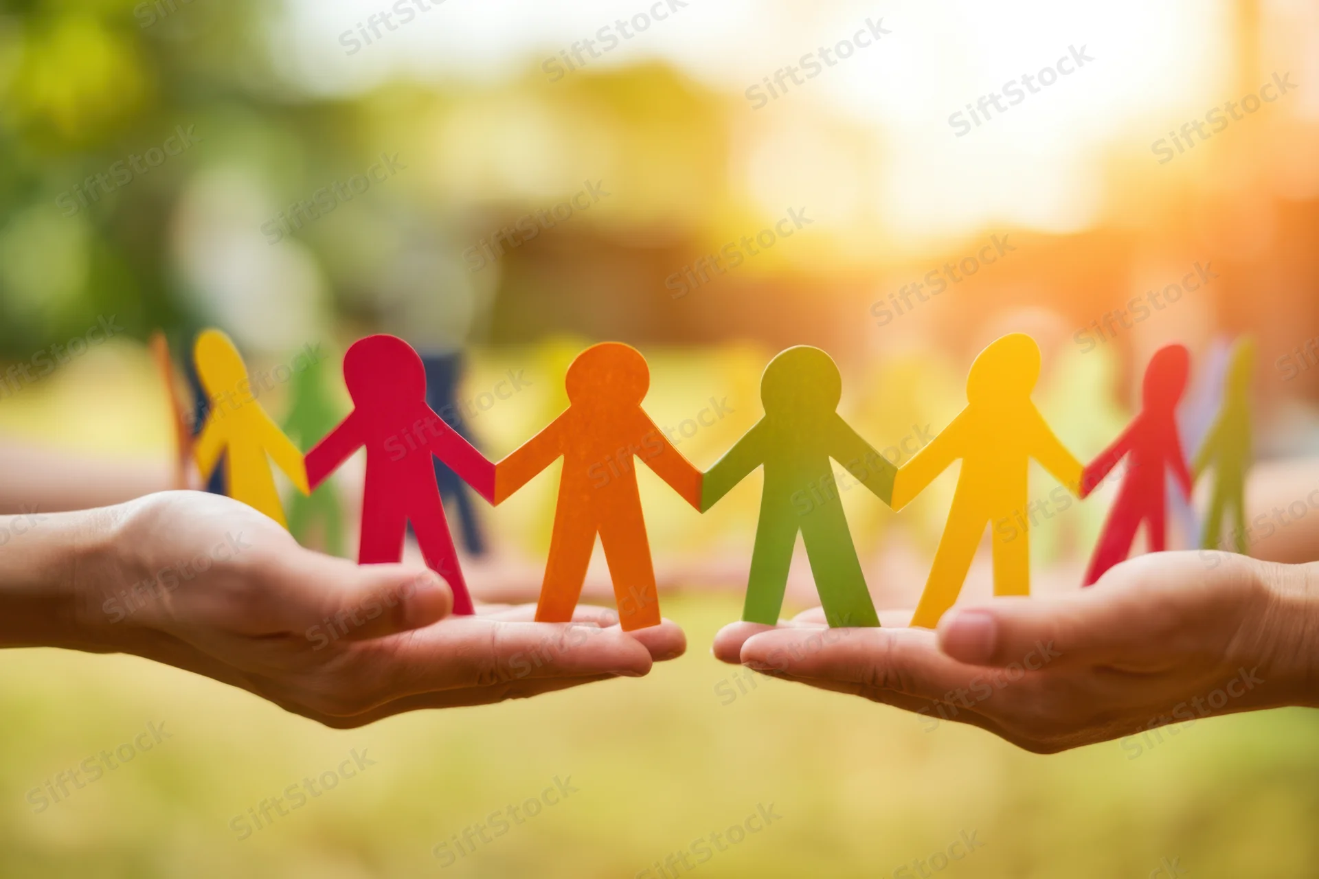 Hands holding a colorful paper chain of connected human figures outdoors in sunlight
