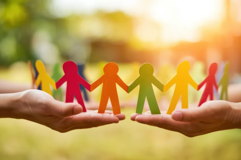 Hands holding a colorful paper chain of connected human figures outdoors in sunlight