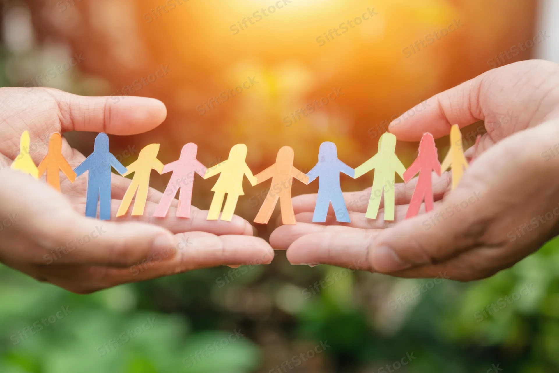 Hands cradling a colorful paper chain of connected human figures outdoors