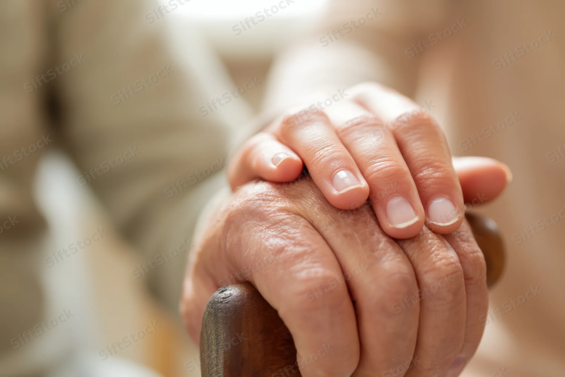 Elderly hand gripping a wooden cane with a younger hand resting on top for support