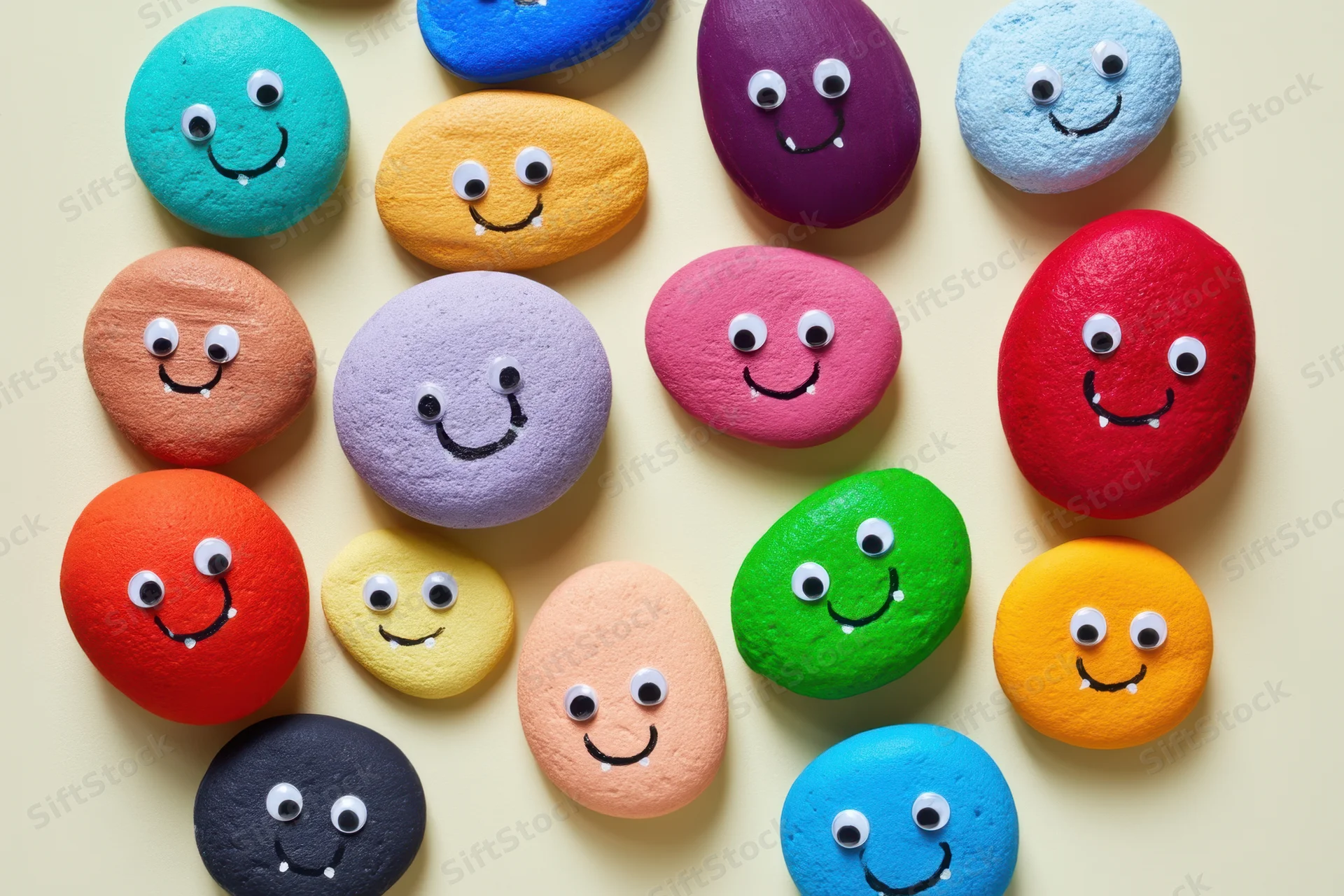 Colorful painted stones with monster faces arranged on a beige surface