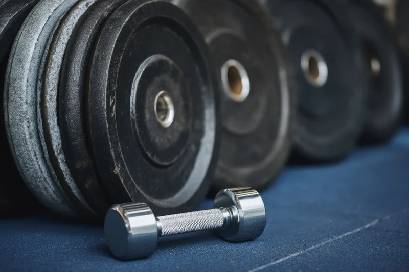 Metal dumbbell resting in front of stacked weight plates on blue gym floor