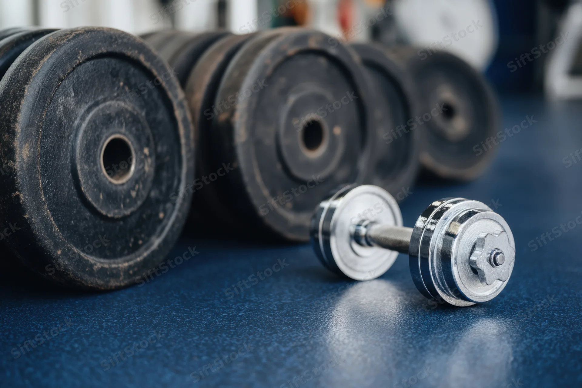 Metal dumbbell and weight plates arranged on blue rubber gym floor