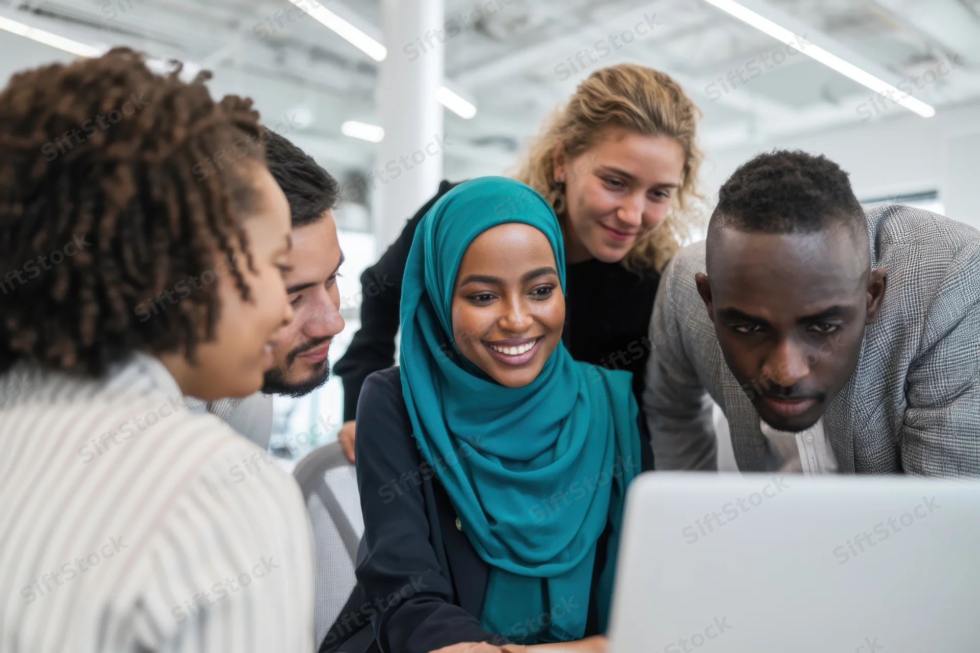 Diverse team of professionals collaborating around a laptop in a bright modern office