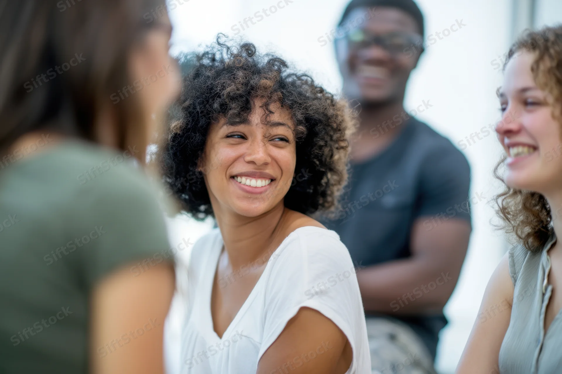 Woman smiling during a casual conversation with friends in a bright indoor setting