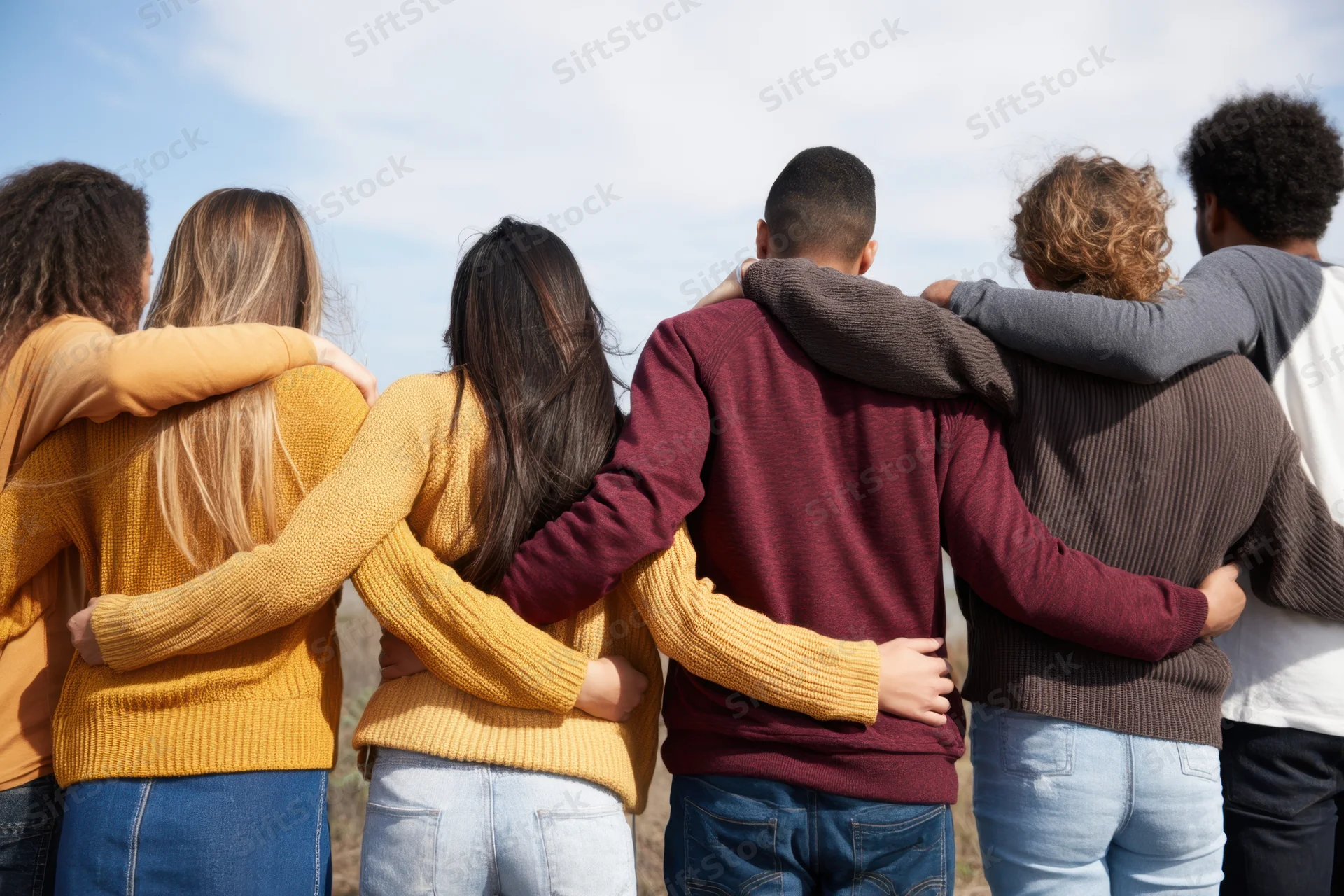 Diverse group of friends standing back to back with arms around each other outdoors