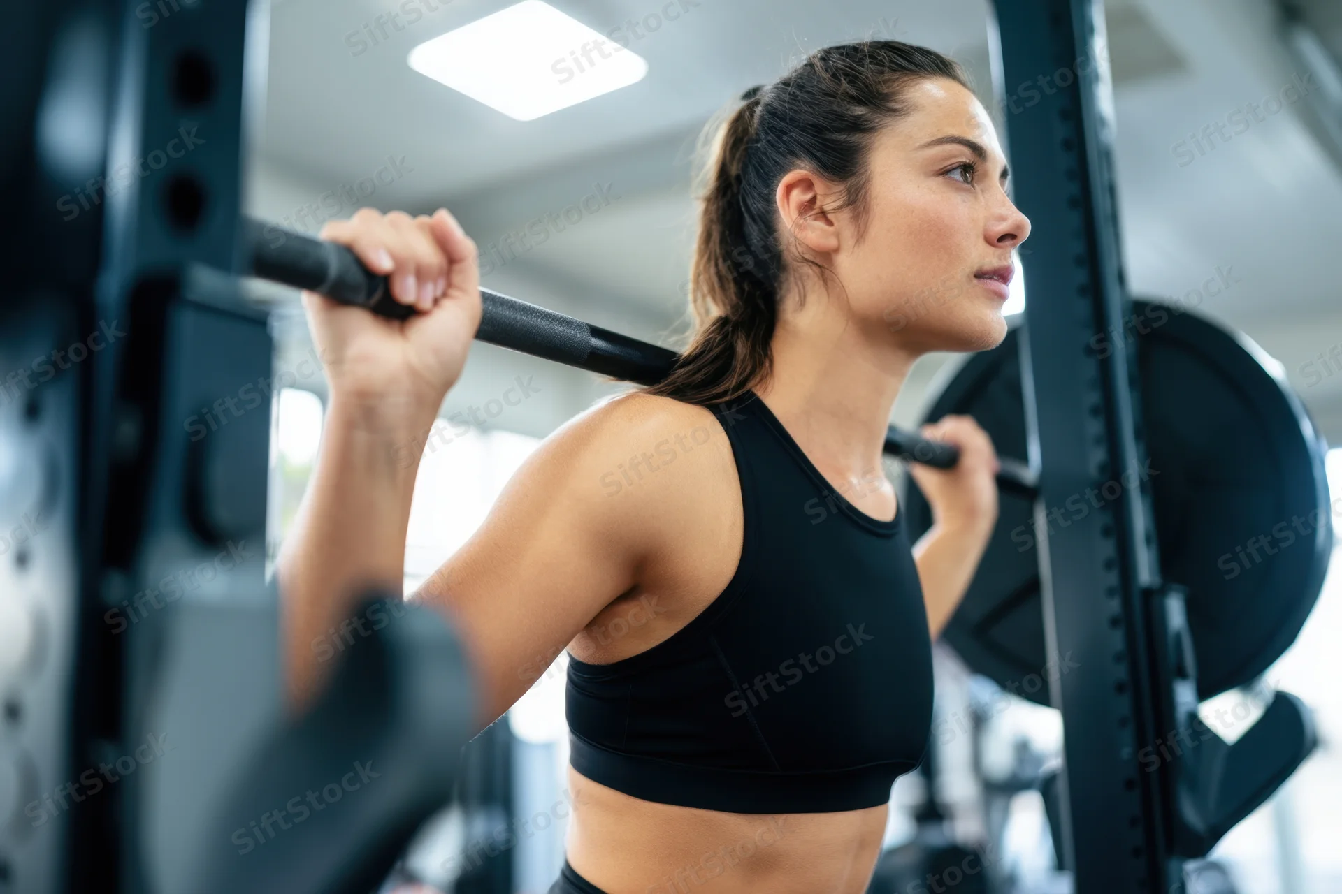 Woman lifting barbell in gym wearing black sports bra, focused expression during strength training