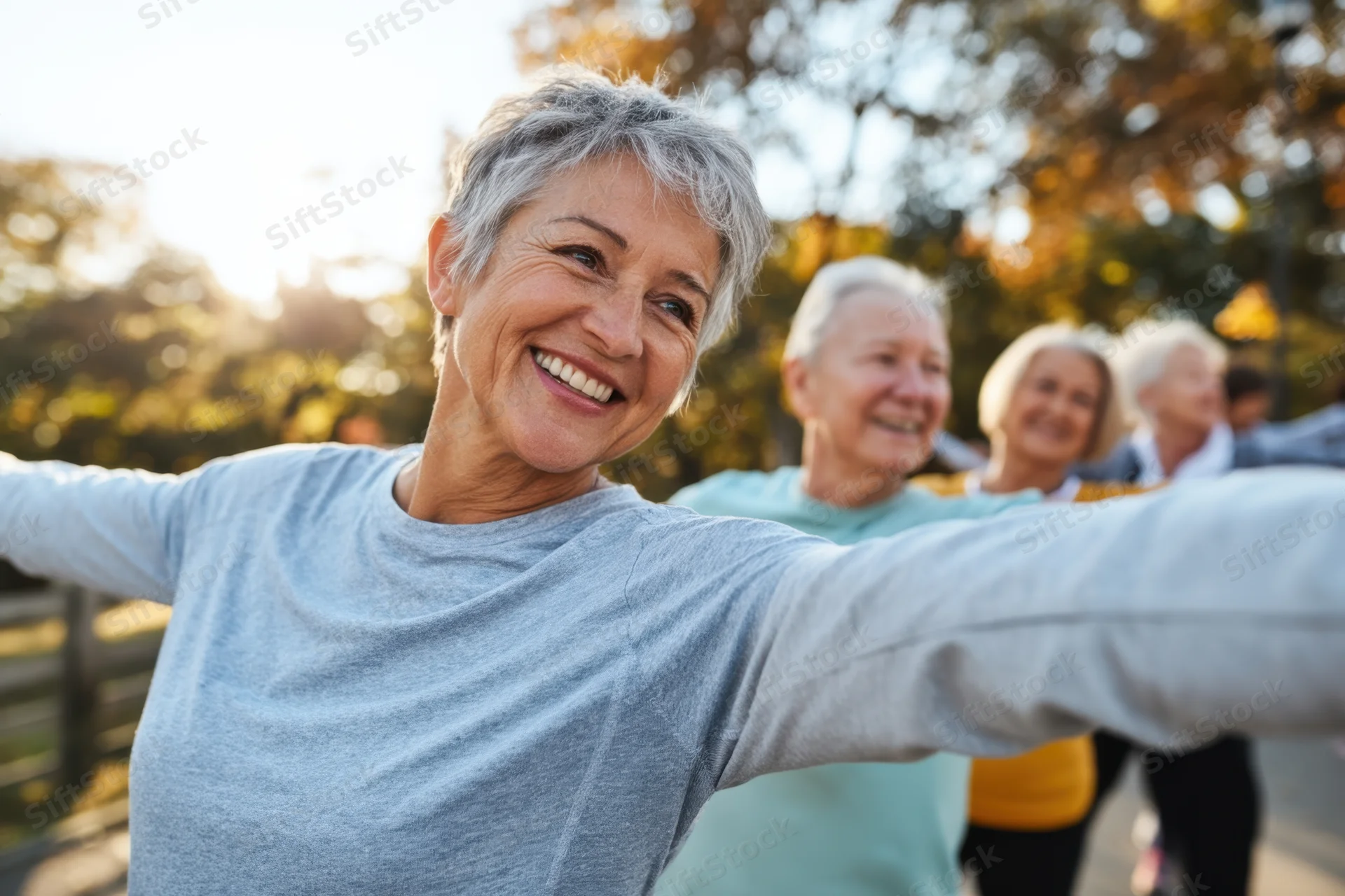 Senior woman smiling with arms outstretched during group exercise in a park