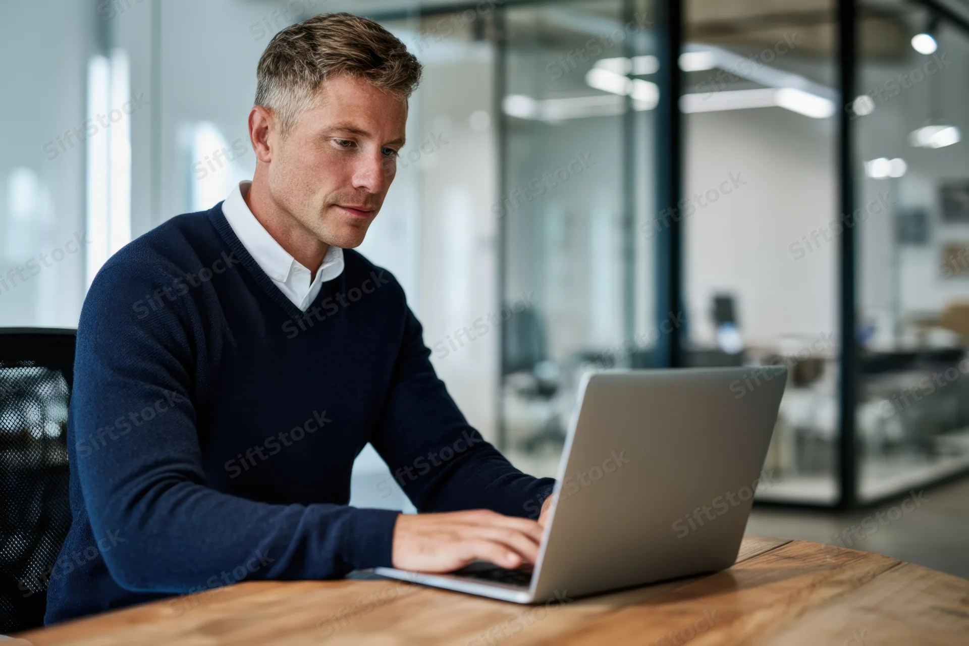 Man typing on laptop at wooden desk in modern office space